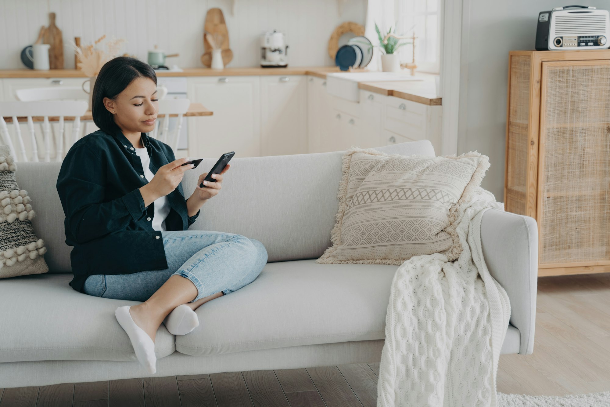 Woman holding banking card, phone making cashless payment sitting on couch at home. Online banking Woman holding banking card, phone making cashless payment sitting on couch at home. Online banking