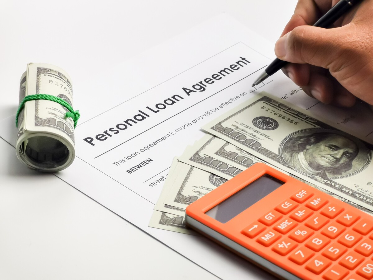 Filling up personal loan agreement form with a pen, calculator and fake money.