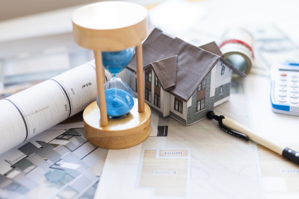 Wooden house and clock. Businessman counting money. Payment of deposit or advance payment for